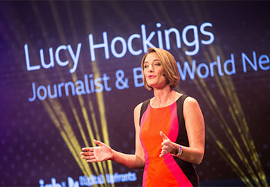 BBC Journalist, Lucy Hockings, wearing an orange dress and giving an opening speech