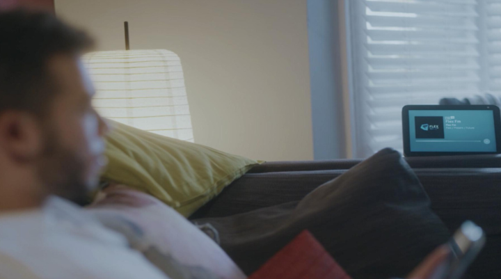 Man in living room on sofa with an Amazon smart speaker in the background 