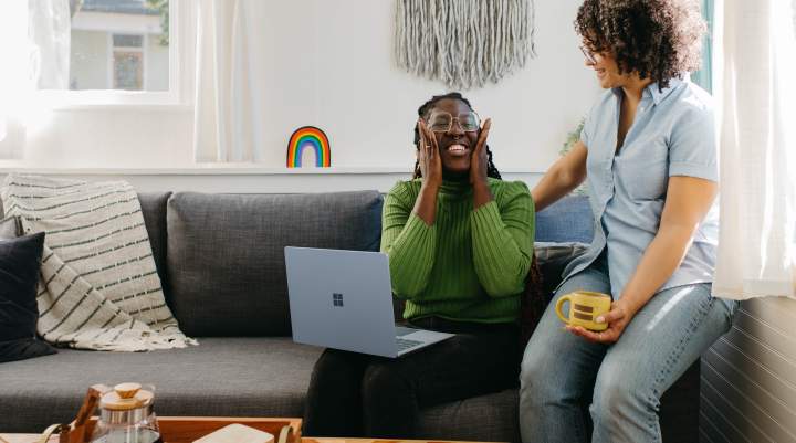 Two women have a conversation, one has a laptop on her knee