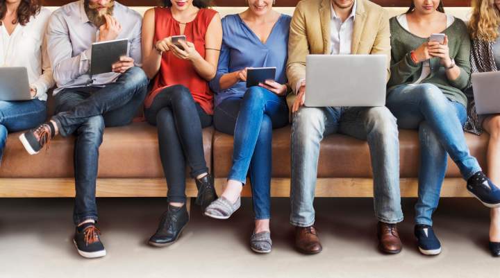 Row of people sat using a range of devices - laptops, ipads, phones. 