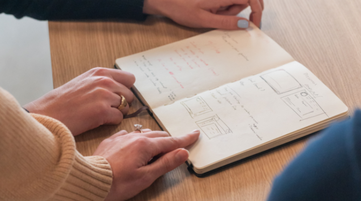 A picture of people's hands pointing at a notebook on a table