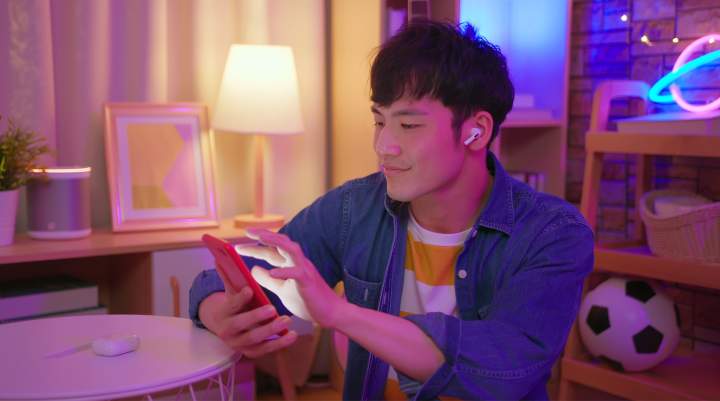 A young man enjoying playing a game on their mobile phone, while listening to an audio ad