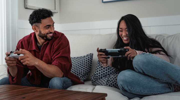 A man and woman play console and handheld games together on a couch.