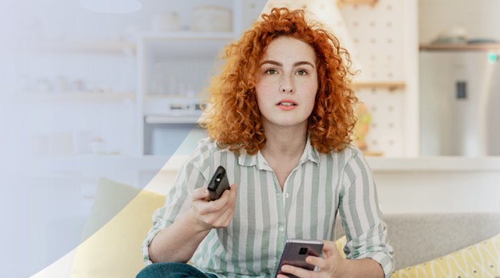 A women holding both her phone and tv remote 